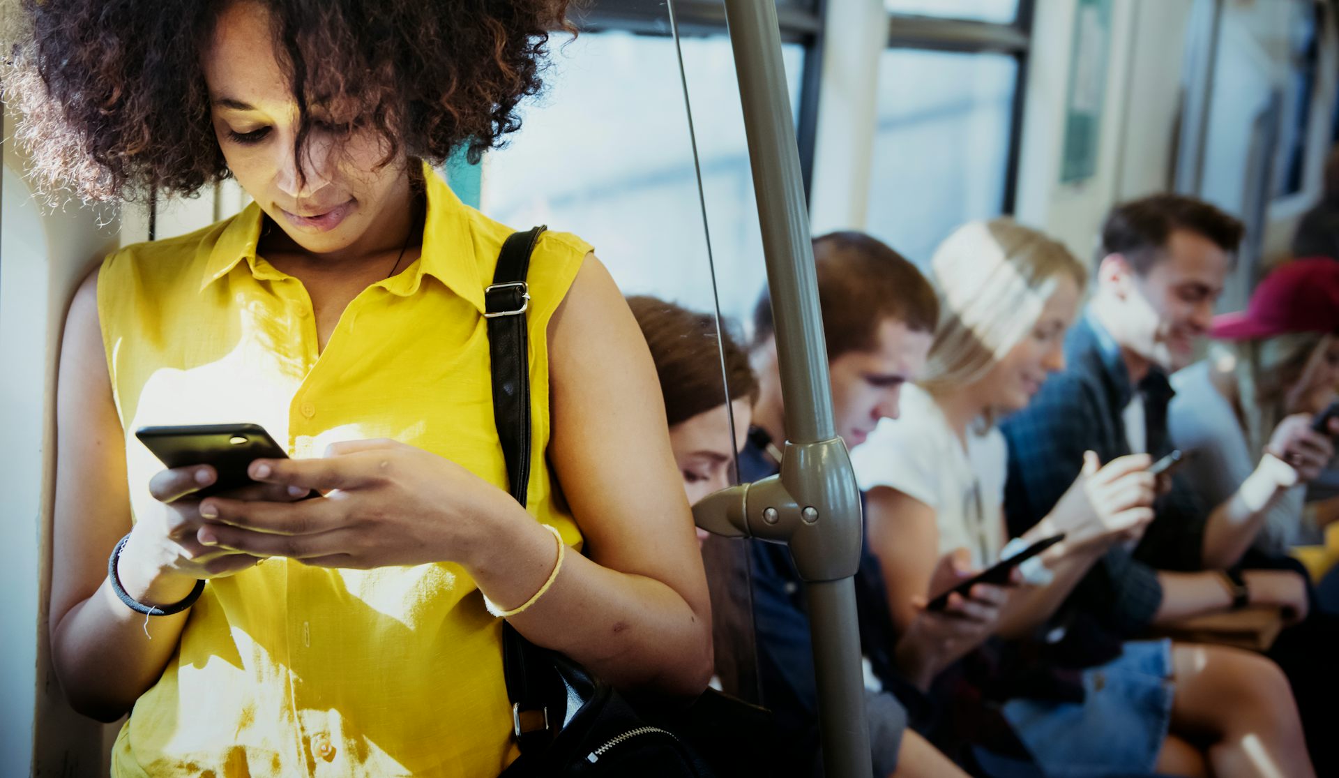 A young woman types on a smartphone while standing on a transit bus