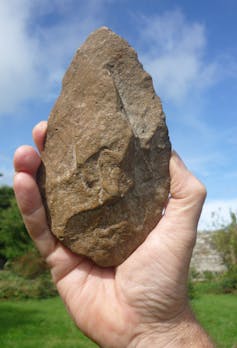 A hand holds an ancient stone handaxe