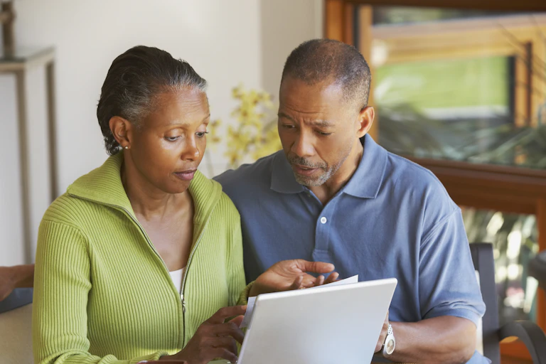 Man and woman with graying hair, looking at a computer, and looking concerned. The woman's left The palm is turned toward the ceiling.