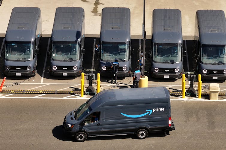 A line of Amazon electric delivery trucks charging while one drives away.
