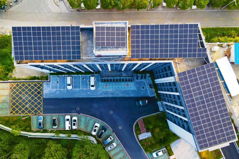 Solar panels cover the rooftop of office towers. Cars are parked below.
