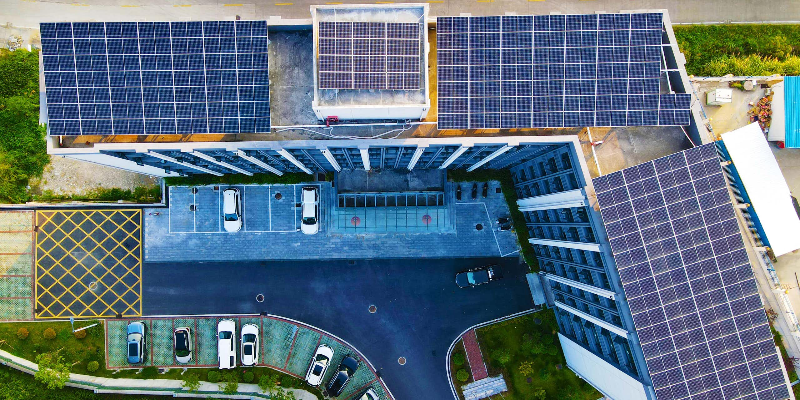 Solar panels cover the rooftop of office towers. Cars are parked below.