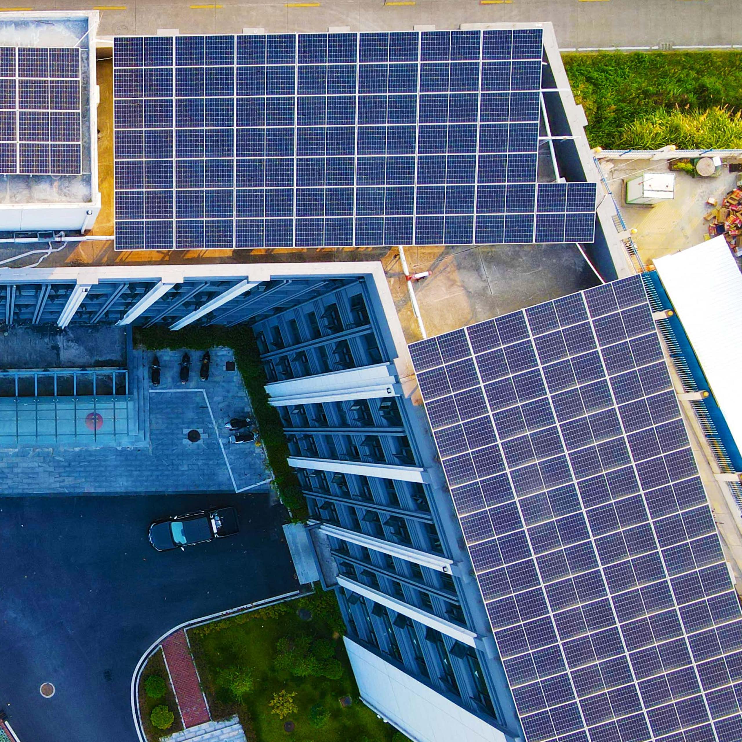 Solar panels cover the rooftop of office towers. Cars are parked below.