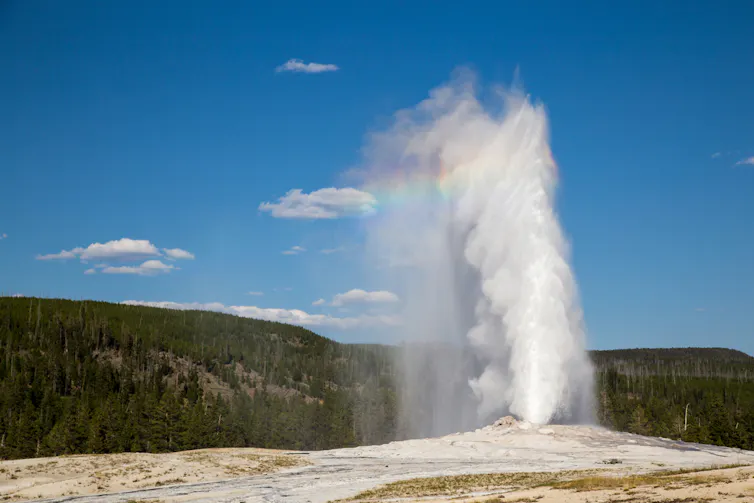 A plume of hot water shoots from the ground against a blue sky backdrop.