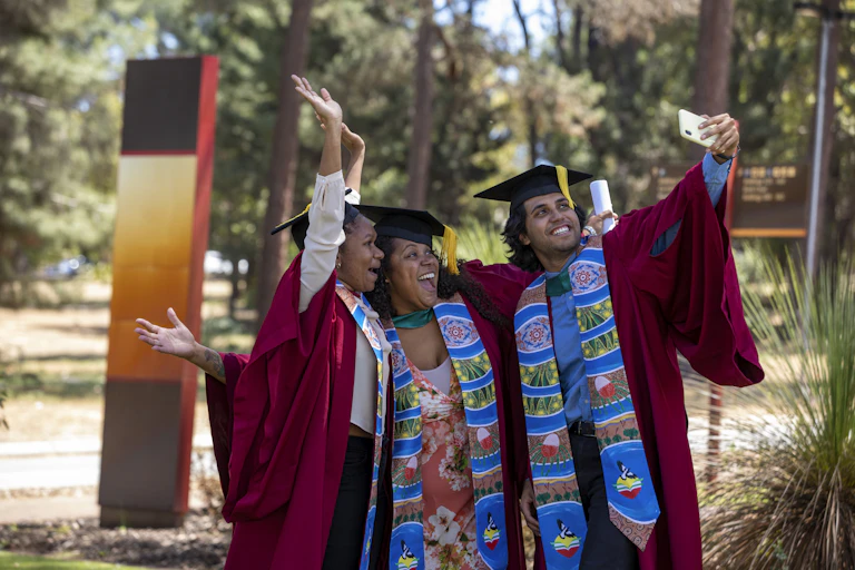 Three Indigenous students taking a selfie, celebrating their graduation.
