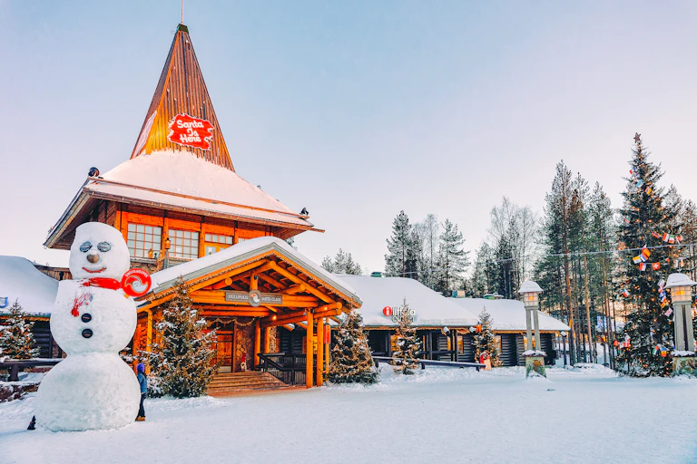 A wooden building covered in snow, reads 'Santa is here'.