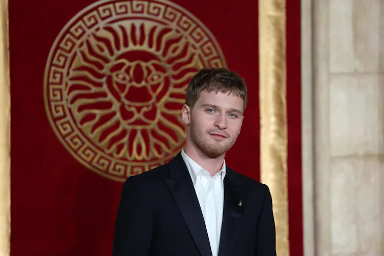 US actor Fred Hechinger plays Caracalla in Gladiator II, he stands on a red carpet in a suit.