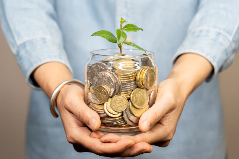 Woman holding jar of money with small green shoot sprouting out of it