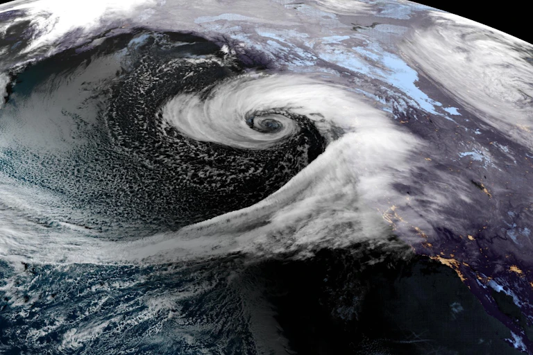 A swirl forms off the coast with a long tail of water vapor pouring into it in this satellite image.