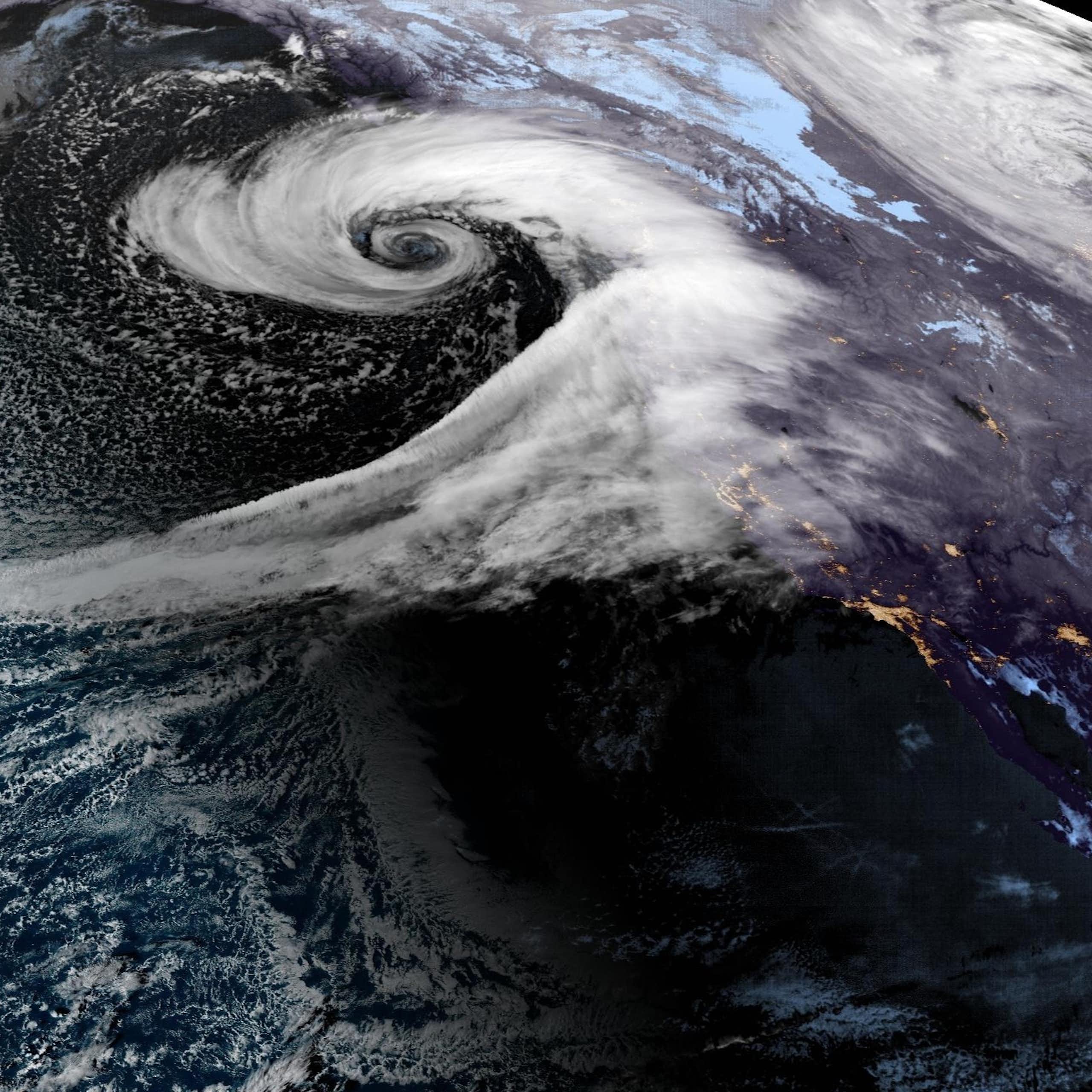 A swirl forms off the coast with a long tail of water vapor pouring into it in this satellite image.