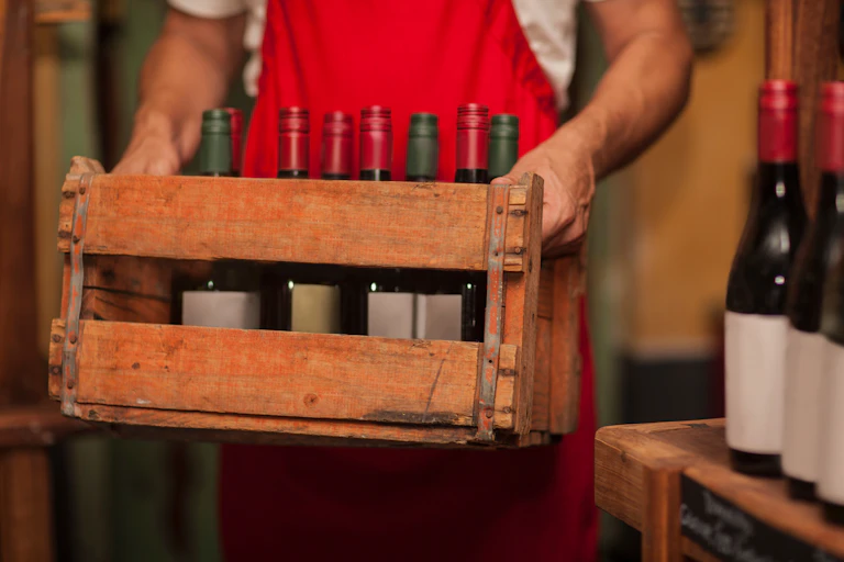 A man holds a wooden crate with bottles of wine in it.