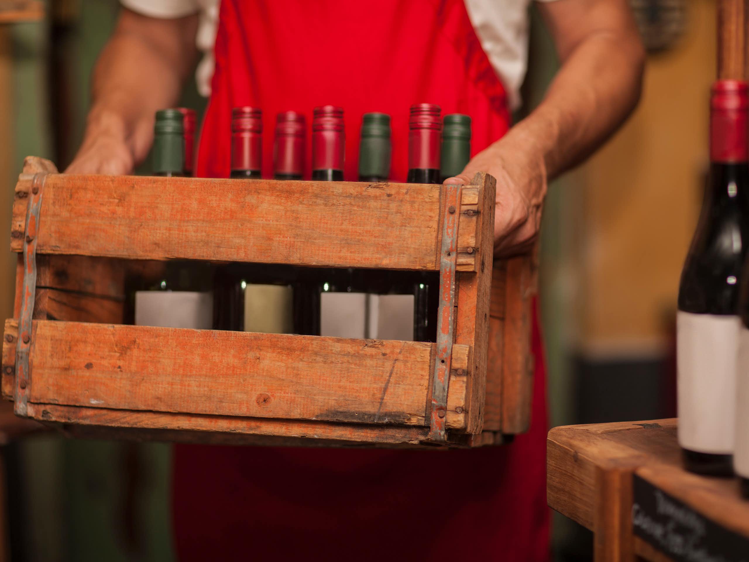 A man holds a wooden crate with bottles of wine in it.