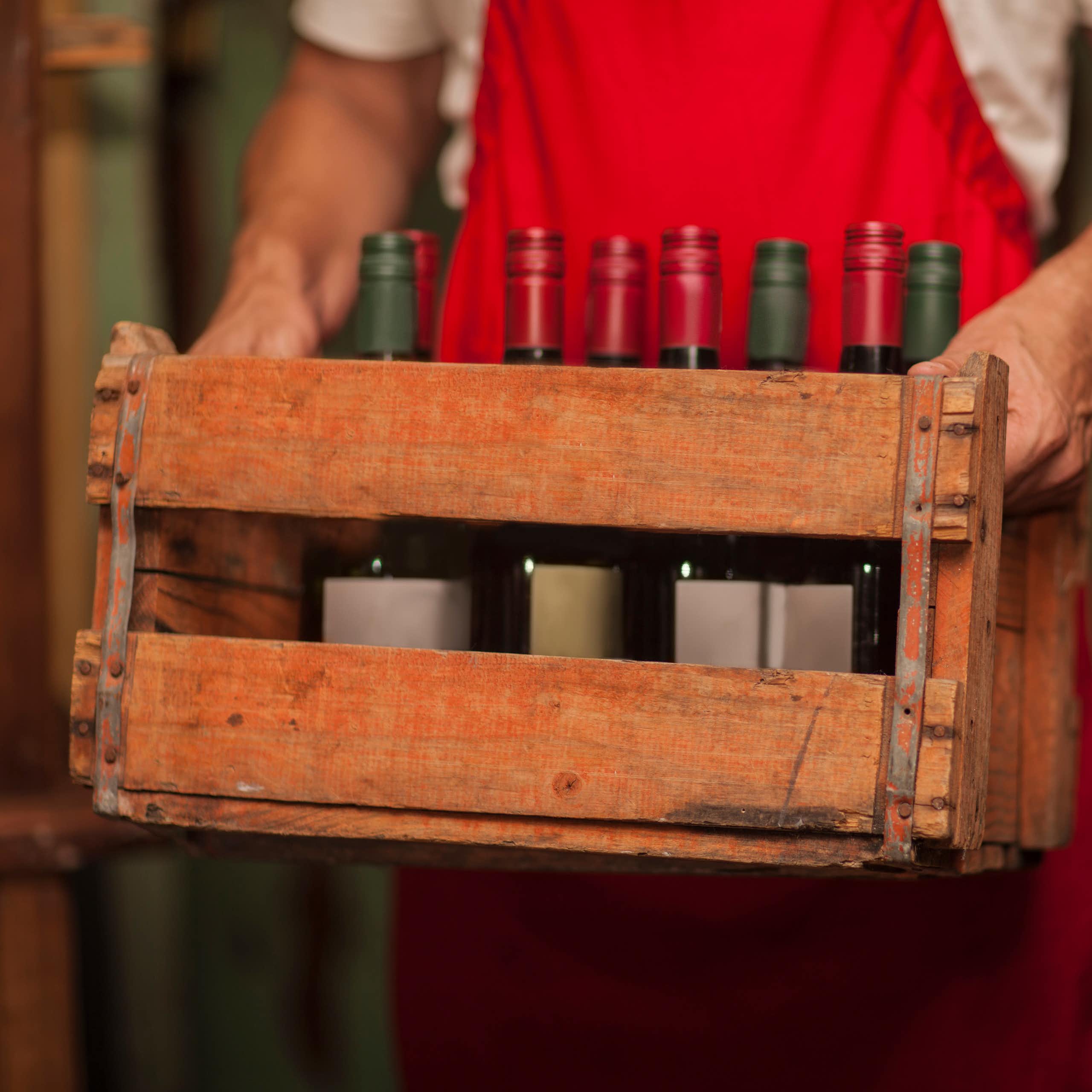 A man holds a wooden crate with bottles of wine in it.