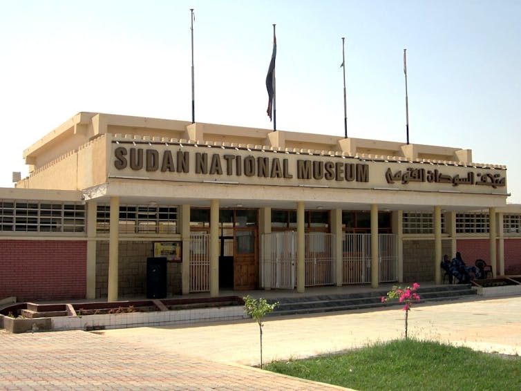 A flat building with columns along the front and flags flying above it.