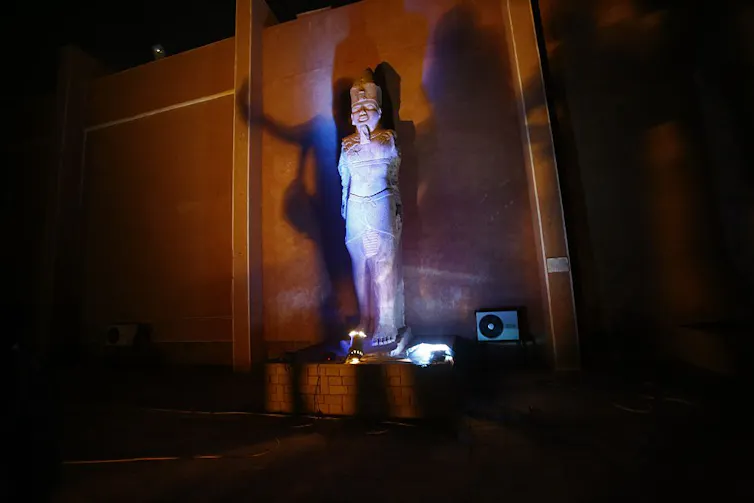 A statue of an ancient king in an alcove, lit up by lights.
