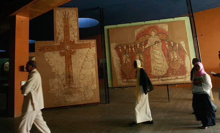 People walk past large artworks featuring crosses and priests.