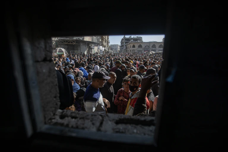 Men, women and children stand outside a small swuare window where bread is being distributed.