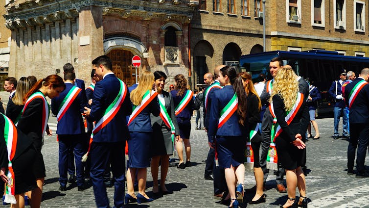 um grupo de pessoas conversando, todas usando faixas com as cores da bandeira italiana.