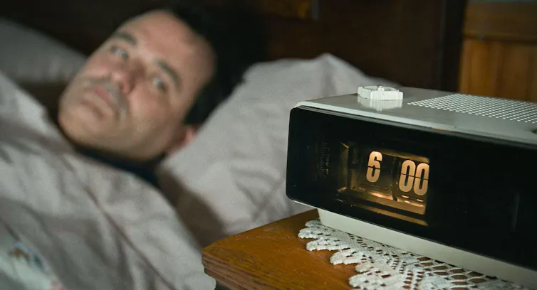 Bill Murray looks at a clock which reads 6.00.