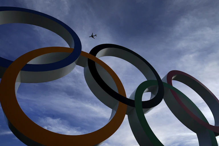 A passenger jet is seen flying over the five Olympic rings.