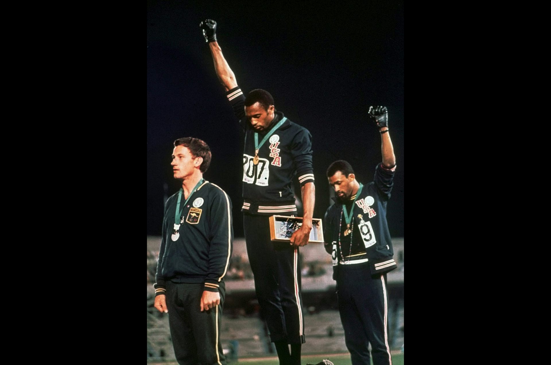 Two black men on a medal podium raise their fists and bow their heads.