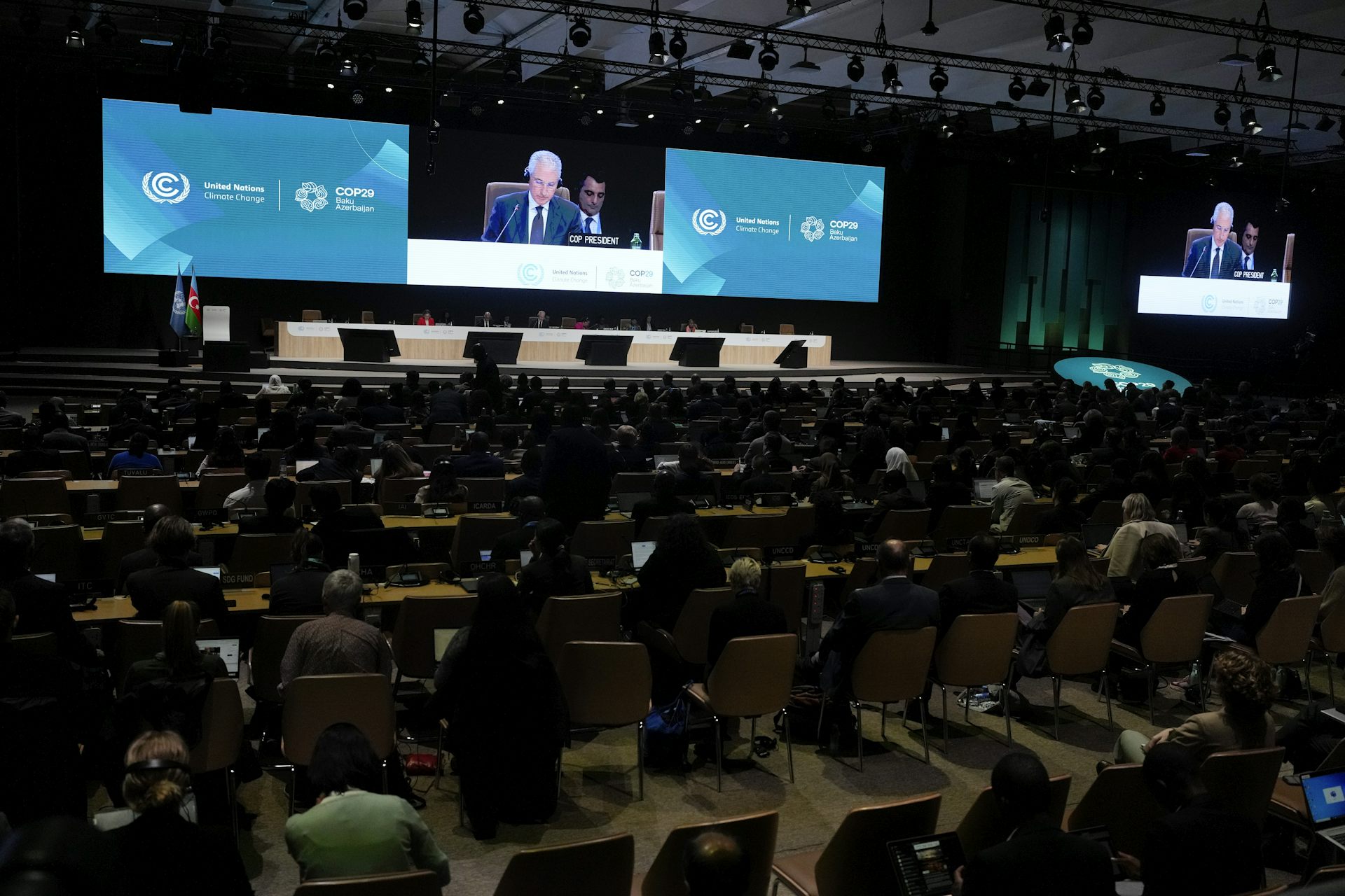 A room full of people sit at tables while a man speaks at a podium.