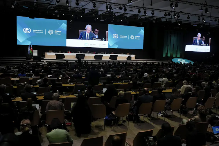 A room full of people sit at tables while a man speaks at a podium.