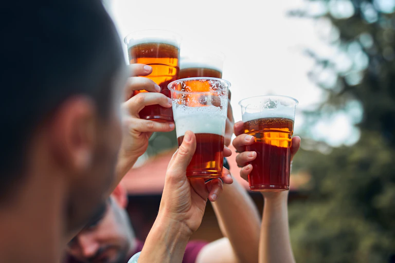 Close up of hands holding glasses of a foamy, amber-coloured beverage knocking their cups together