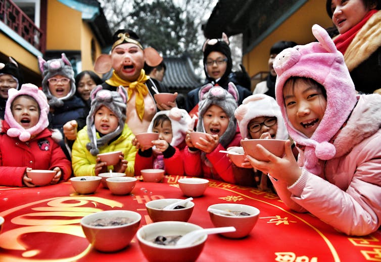 Children, wearing bunny hats, seated around a table with a red table cloth, with several bowls on it.