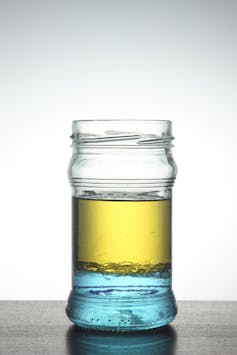 A jar filled with oil and water, with the oil settling on top in a layer.