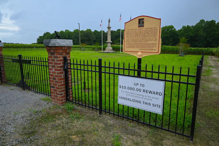 Photo of a small monument on a patch of green grass, fenced in