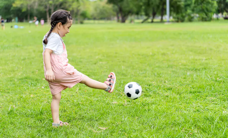 A young girl kicking a soccer ball on a open field