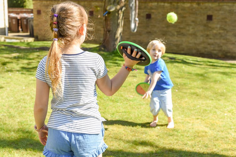 Two children playing catch with a tennis ball and velcro paddles