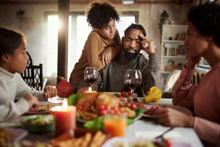 Boy consoling his father while having a holiday meal with their family at dining table.