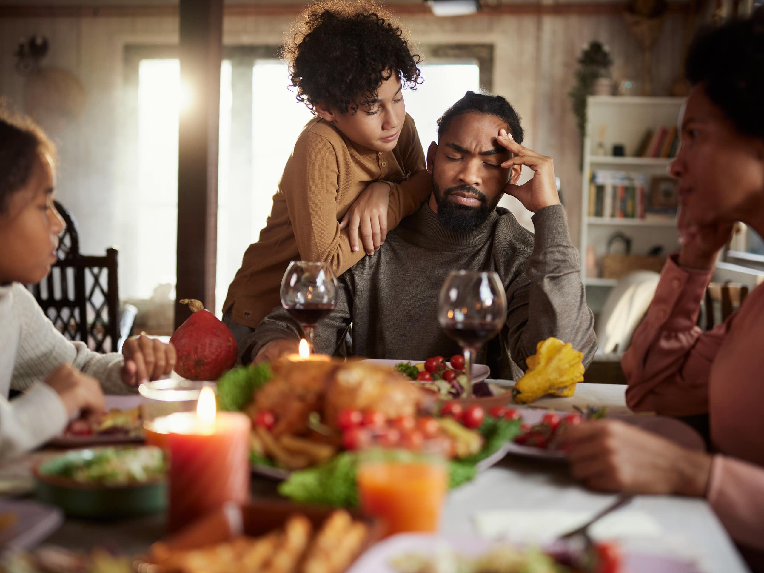 Boy consoling his father while having a holiday meal with their family at dining table.