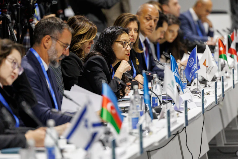 A row of delegates sit at a table, with the middle person speaking..