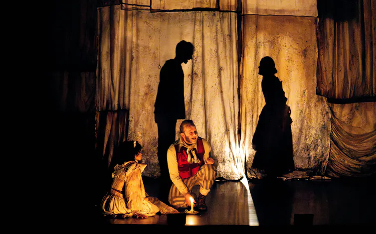 Two people on stage, shadow puppets behind them.