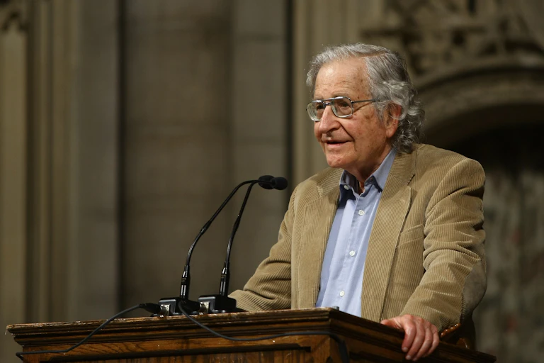 an older man wearing glasses stands at a lectern