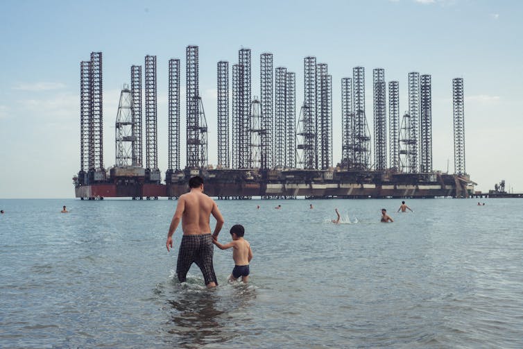 A man and son at beach with oil refineries behind