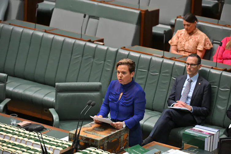 Woman wearing blue dress speaking at a lectern.