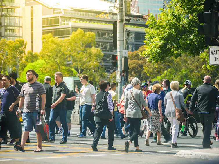 People cross a busy street in lined with trees in Melbourne.