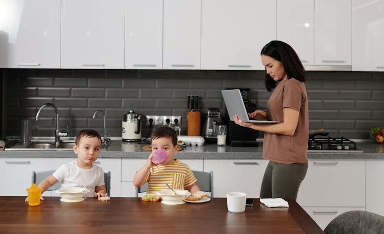 Woman walks in kitchen with laptop