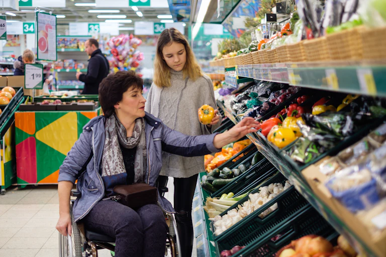 une personne en fauteuil roulant devant le rayon fruits et légumes d'un grand magasin
