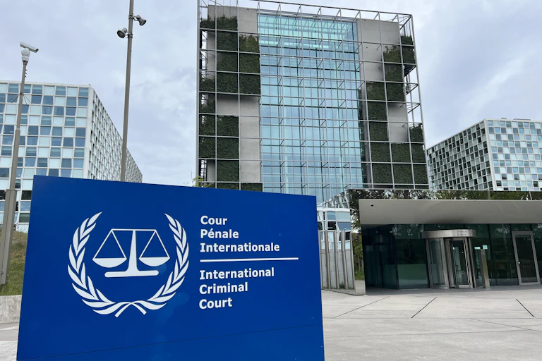 A building with lots of glass windows is seen behind a sign with the scales of justice depicted.