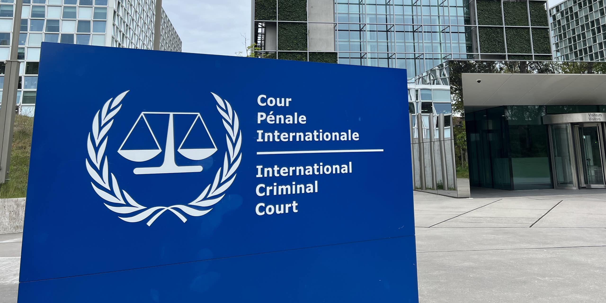 A building with lots of glass windows is seen behind a sign with the scales of justice depicted.