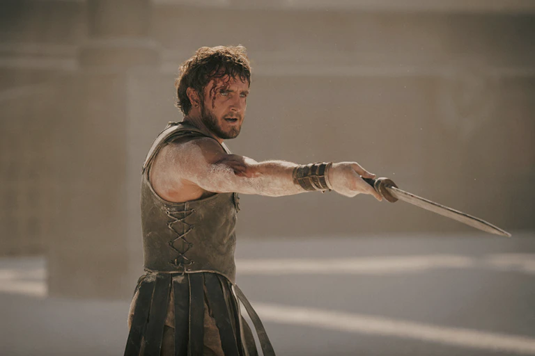 Young bearded man with blood dripping down his face dangles a sword with his outstretched arm.