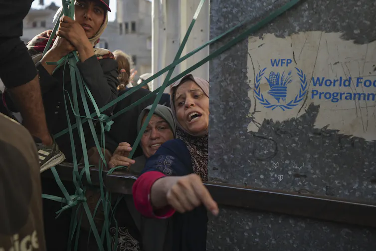 Women in crowd around a gate with a sign for the World food programme