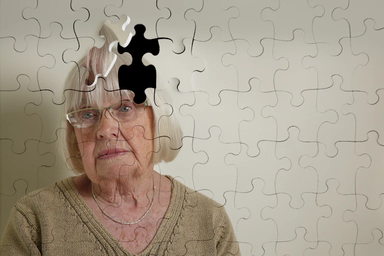 Senior woman's face looking forlorn, reflected on a jigsaw puzzle with a missing piece.