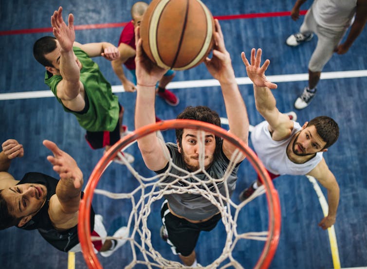 An above-court photograph of several men playing basketball, with one man about to dunk the ball through the hoop.