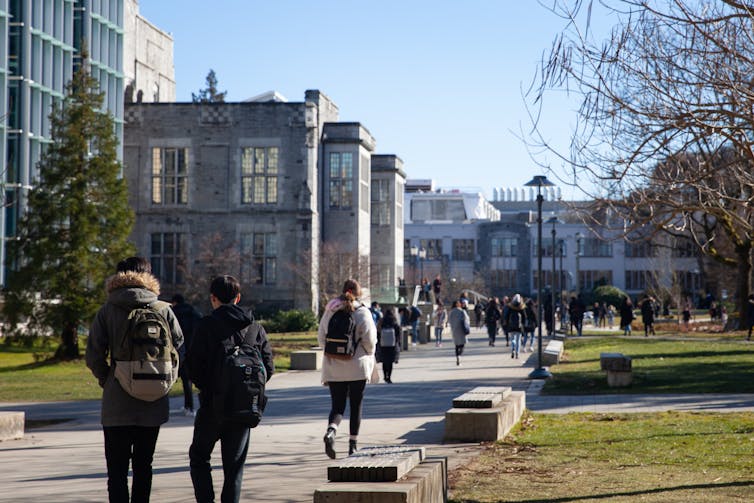 People wearing backpacks walk along a path near buildings.